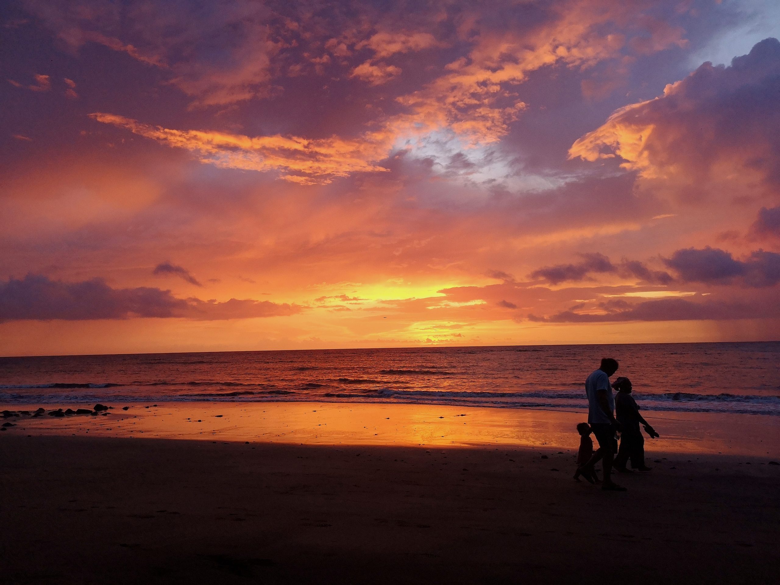 Une famille marche sur la plage de Bouéni face au coucher de soleil